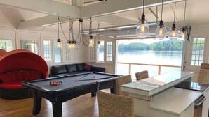 Une table de billard avec un queue de billard, une chaise rouge et un coin repas avec des chaises en osier.