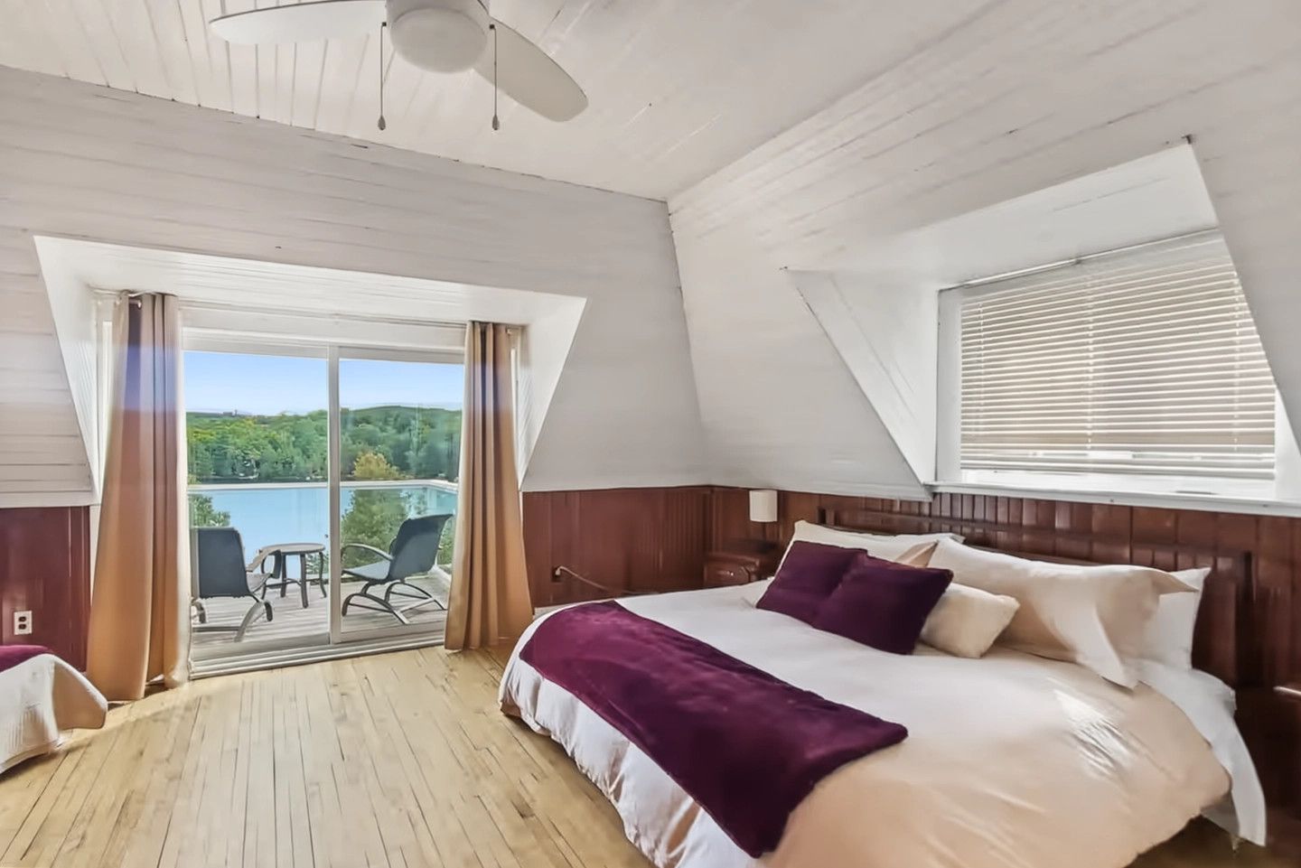 A bedroom with a large bed, a view of a balcony, and a window with blinds.