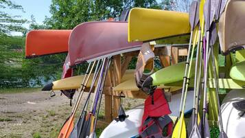 Une collection de canoës et de kayaks de différentes couleurs, notamment rouge, jaune, vert et blanc, appuyés contre une structure en bois.