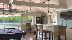Une table de billard avec des chaises, un coin bar avec des tabourets en osier et un téléviseur fixé au mur.
