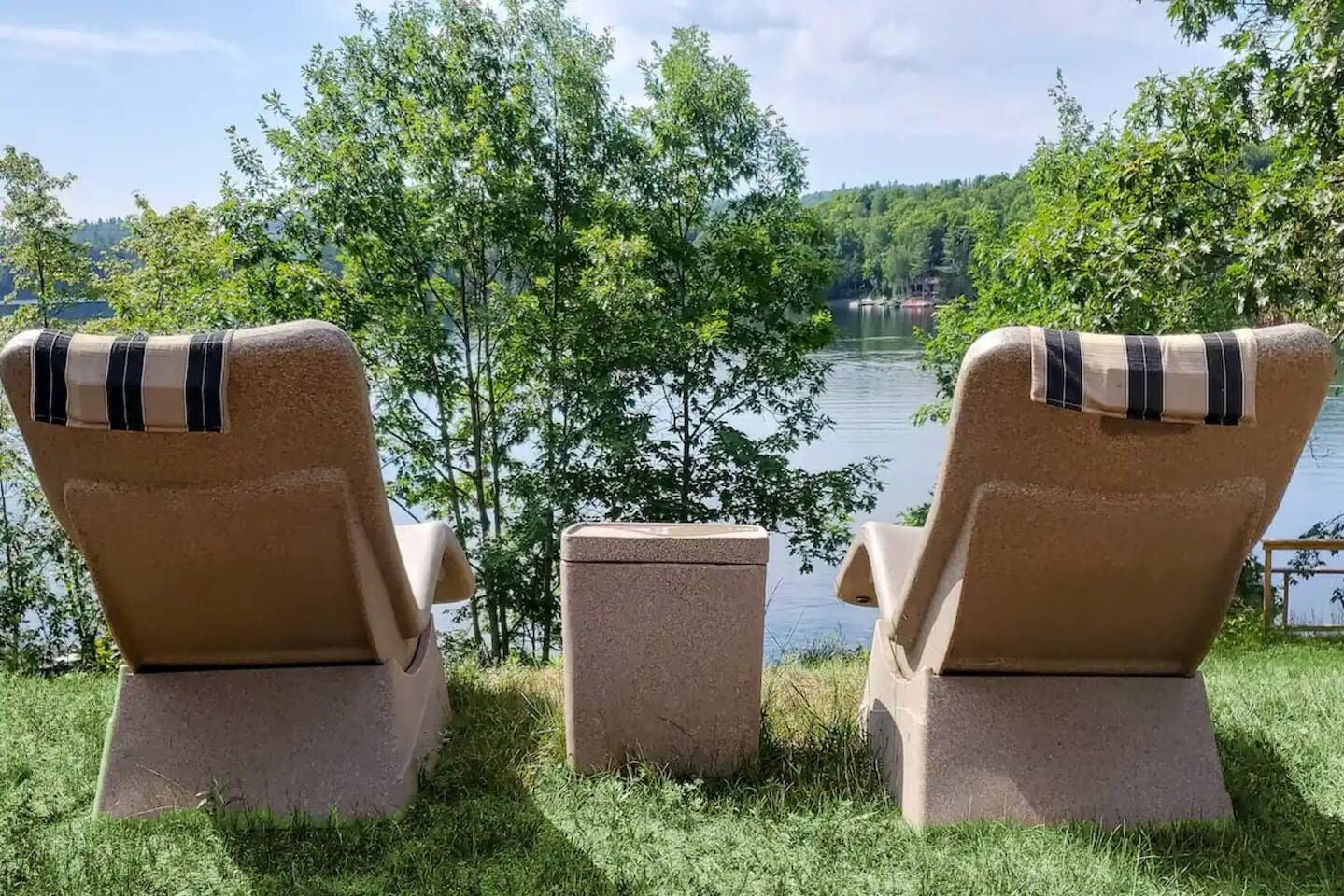 Zwei Liegestühle im Freien mit Blick auf einen See, dazwischen ein kleiner Tisch.