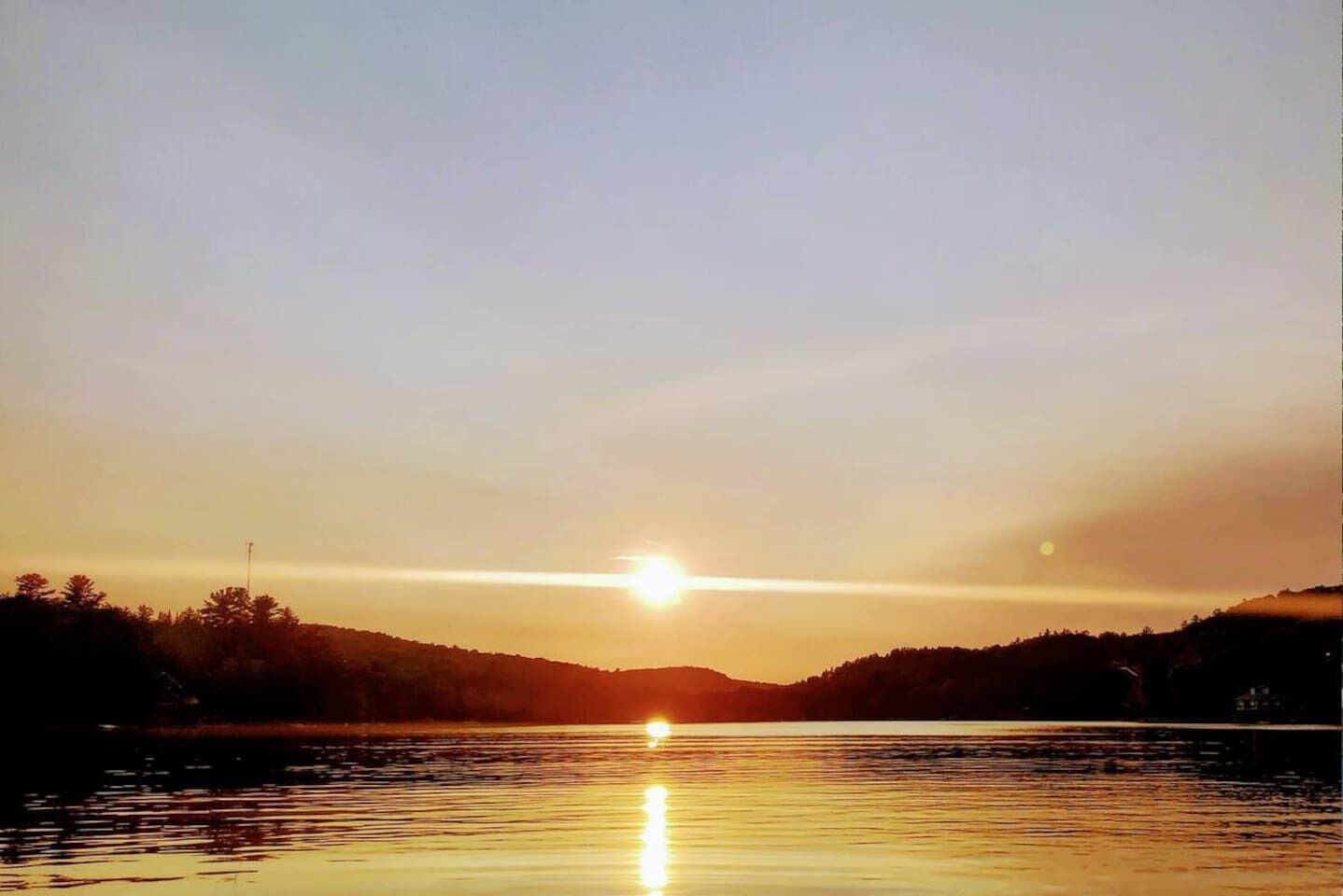 Un coucher de soleil sur une étendue d’eau calme, avec la silhouette de collines en arrière-plan.
