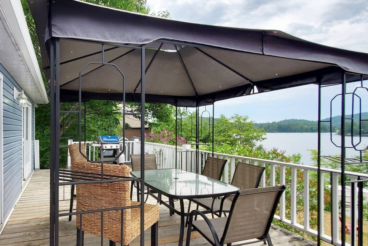 Un área de comedor al aire libre techada con mesa y sillas, con vista a un lago.