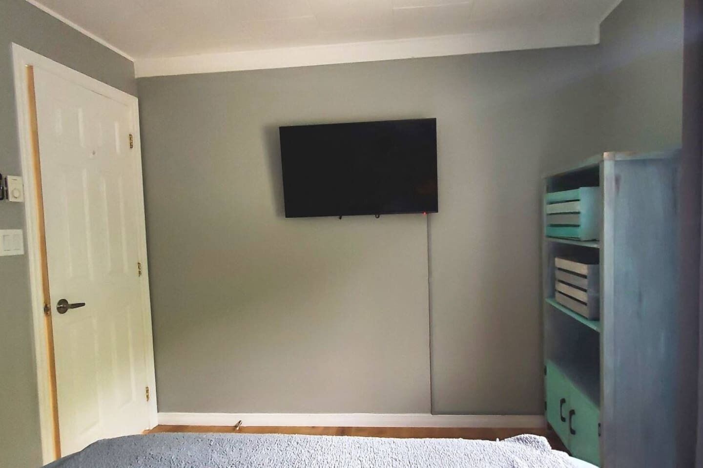Une pièce avec une porte, un téléviseur fixé au mur et une étagère.