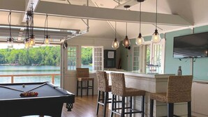 Une table de billard avec des chaises, un coin bar avec des tabourets et un téléviseur fixé au mur.