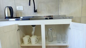 Una cocina compacta con un lavamanos, una tetera y estantes de almacenamiento.