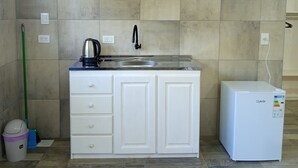 Una cocina con encimera blanca, un lavabo, una tetera y un refrigerador.