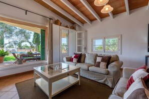 Un salon avec une table basse en verre, un canapé, une fenêtre donnant sur l’extérieur et un plafond avec des poutres en bois.