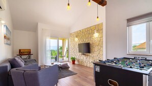 Una sala de estar moderna con una mesa de fútbol de mesa, un sofá, un televisor montado en una pared de piedra y un balcón con vistas.