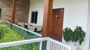 Een overdekt terras met een glazen balustrade, houten pilaren en een deur met raam.