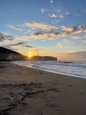 A beach with waves, a sunset, and a distant building. - EXCELLENT LOCATION, 50 M FROM THE BEACH, 3-BEDROOM APARTMENT (Algajola)