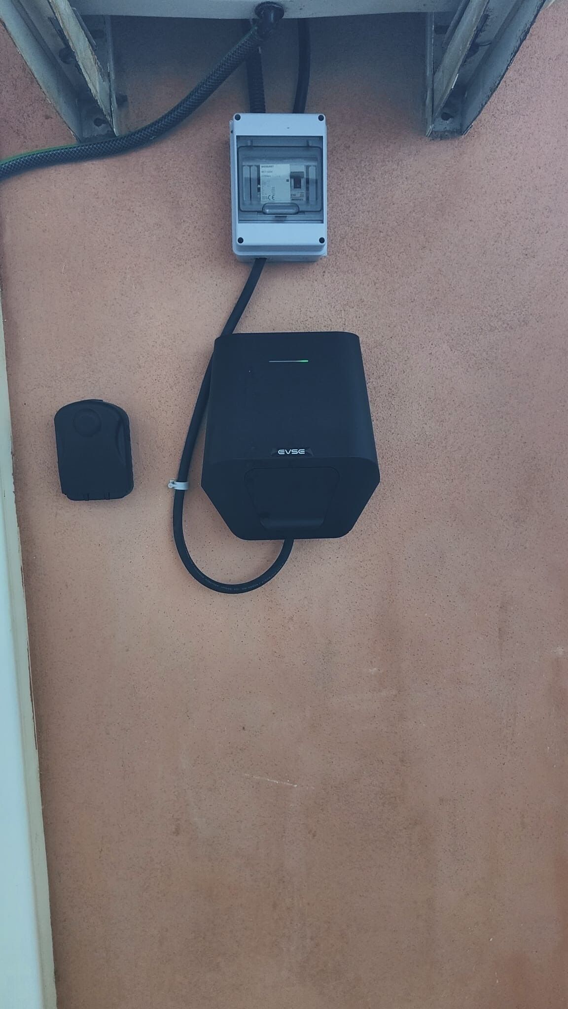 Eine Mehrfachsteckdose mit einem schwarzen Gerät und einer weißen Steckdosenleiste an einer beigen Wand.