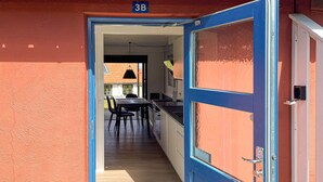 Puerta abierta que da a una habitación con comedor, cocina y el número '3B' a la vista en la pared.