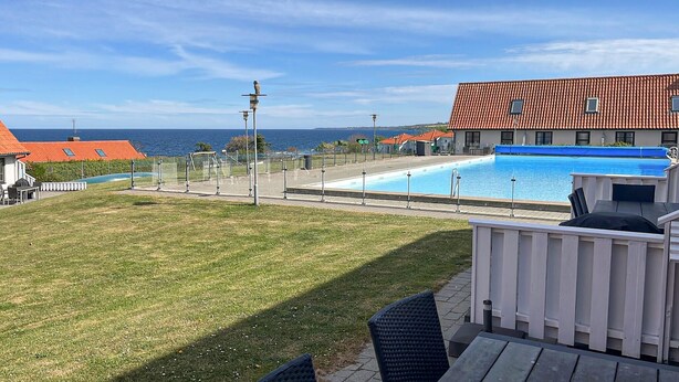 Una piscina con vista al mar, un área cercada y un edificio con techo rojo.