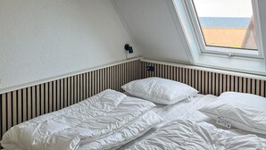 Una habitación pequeña con cama individual, techo inclinado y ventana con vista a la playa.