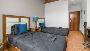 Ein Hotelzimmer mit zwei Betten, Holz-Kopfteilen, Holzboden, Holztür und einem Metallstuhl.