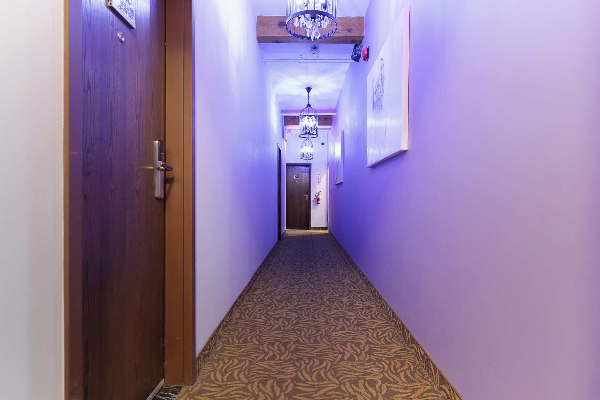 A hallway with patterned carpet, wooden doors, and a chandelier.