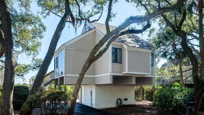 A modern two-story house with a flat roof, surrounded by mature trees and a well-maintained garden. - 2BR/2BA + Loft Cottage! Close to Beach! Golf Course Views! Amenity access Available! (Seabrook Island)