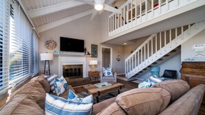 A spacious living room with a high ceiling, a fireplace, a large TV, and a staircase leading to an upper level. - 2BR/2BA + Loft Cottage! Close to Beach! Golf Course Views! Amenity access Available! (Seabrook Island)