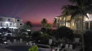 Un resort con piscina, sillones de descanso y vista al océano al atardecer.
