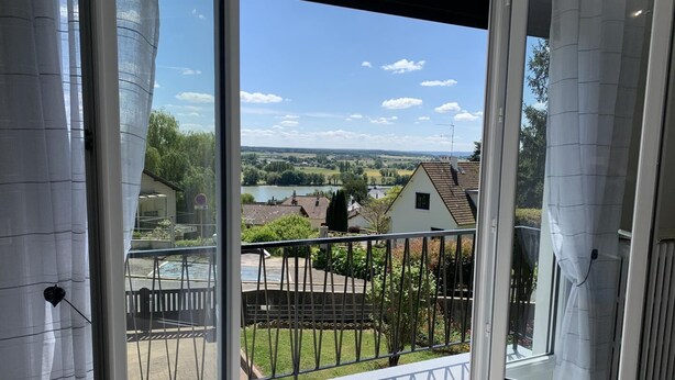 En balkon med udsigt over et sølandskab, huse og et fjerntliggende landskab.
