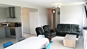 En moderne stue med sofa, stole, spisebord og et køkken med hårde hvidevarer.