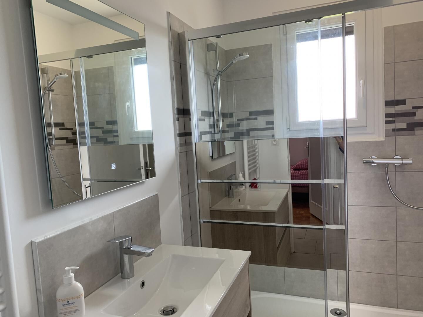 Un baño moderno con ducha de vidrio, un espejo grande y un lavamanos blanco.