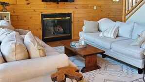 A cozy living room with a wooden ceiling, a fireplace, a television, and a staircase. - Rock Lake Retreat: Sun, Water & Relaxation – The Ultimate Summer Escape! (Iron Mountain)