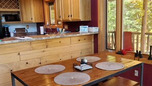 A modern kitchen with wooden cabinets, a granite countertop, and a large dining table with placemats. - Rock Lake Retreat: Sun, Water & Relaxation – The Ultimate Summer Escape! (Iron Mountain)
