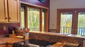 A kitchen with wooden cabinets, a stove, granite countertops, and large windows with a view of trees. - Rock Lake Retreat: Sun, Water & Relaxation – The Ultimate Summer Escape! (Iron Mountain)