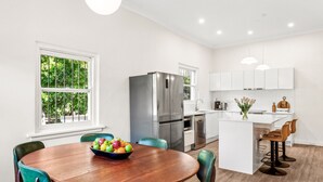 A modern kitchen with white cabinets, stainless steel appliances, and a wooden dining table with chairs. - Tranquil Coogee Retreat with large backyard & pool (Coogee)