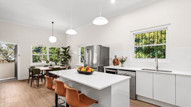 A modern kitchen with white cabinetry, a stainless steel refrigerator, a dining area with a white table and chairs, and a window with a view of greenery. - Tranquil Coogee Retreat with large backyard & pool (Coogee)