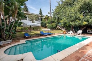 A swimming pool with lounge chairs, a covered patio, and surrounding greenery. - Villa 'Las Cancelas' with sea views, private pool and Wi-Fi (Estepona)
