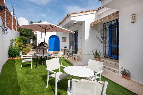 A patio with white chairs and a table, a blue door, and a white wall with a satellite dish.