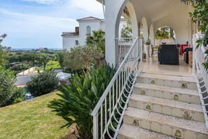 A covered outdoor area with steps leading to a seating area, surrounded by greenery and a view of the landscape.