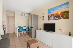 Un salon moderne comprenant un coin repas, un téléviseur à écran plat et un tableau représentant un coucher de soleil sur l’eau.