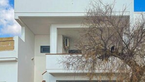 Un bâtiment moderne à deux étages, avec un escalier menant à l’étage supérieur, un arbre devant et un ciel dégagé.
