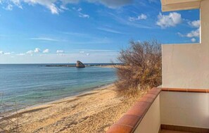 A beach view with a clear sky, a sandy shore, and a distant rock formation.