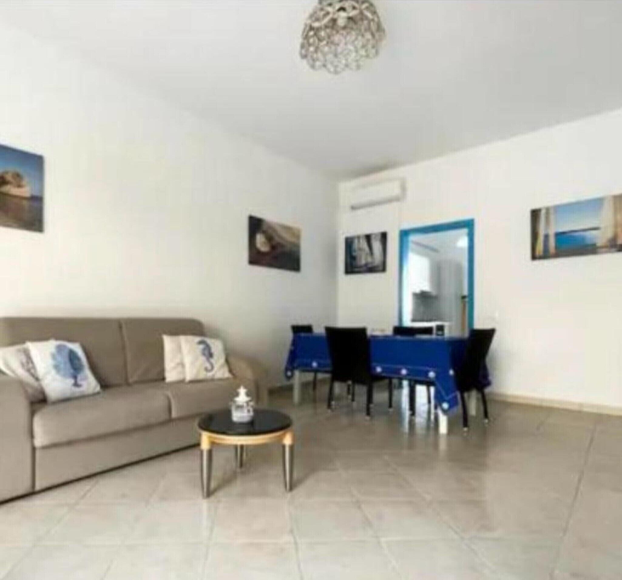 A living room with a sofa, a coffee table, a dining table with chairs, and artwork on the walls.