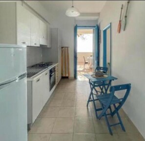 Une cuisine étroite avec des meubles blancs, un fourneau et une table bleue avec des chaises.