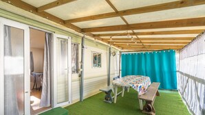 A covered patio with a table and bench, a door leading to an interior room, and a green artificial turf floor. - Mobile home in La Tremblade – Private garden, terrace, playground, and shared pool (La Tremblade (17390))