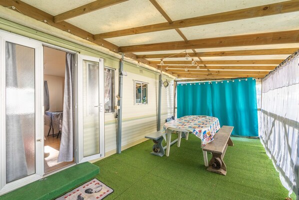 A covered patio with a table and bench, a door leading to an interior room, and a green artificial turf floor.