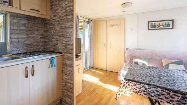 A compact kitchen with a stove, wooden cabinets, and a stone accent wall. - Mobile home in La Tremblade – Private garden, terrace, playground, and shared pool (La Tremblade (17390))