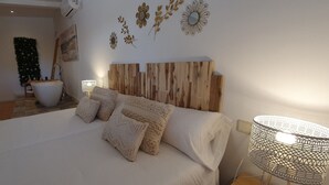 Quarto com cabeceira de madeira, uma cama grande com roupa de cama branca, arte decorativa na parede e um abajur.