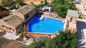 Uma área de piscina com um edifício de pedra, cadeiras de descanso e um espaço coberto para sentar.