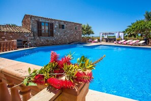 Una piscina con un edificio in pietra e sedie a sdraio sullo sfondo.