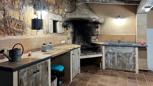 Uma cozinha rústica com parede de pedra, forno de tijolos, armários de madeira e chão de azulejos.