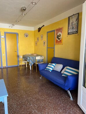 Une pièce avec un canapé bleu, une table à manger avec des chaises, une horloge et une affiche accrochée au mur.