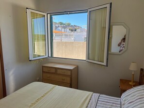Une chambre à coucher avec un lit, une commode, une fenêtre avec des rideaux et un miroir.