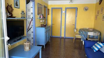 Un espacio habitable compacto con televisión, kitchenette, zona de comedor y sofá.